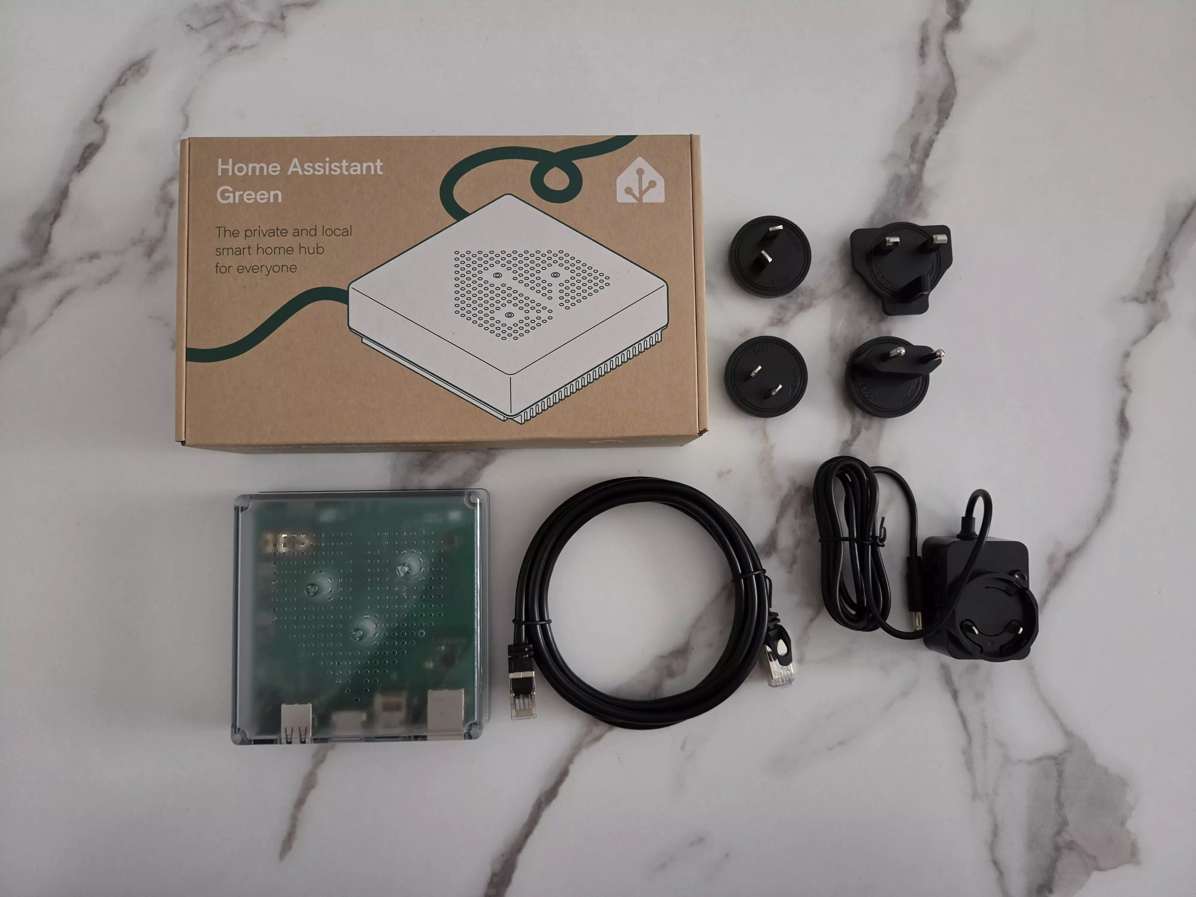 Home Assistant Green avec sa boîte, son alimentation, ses adaptateurs secteur et son câble Ethernet