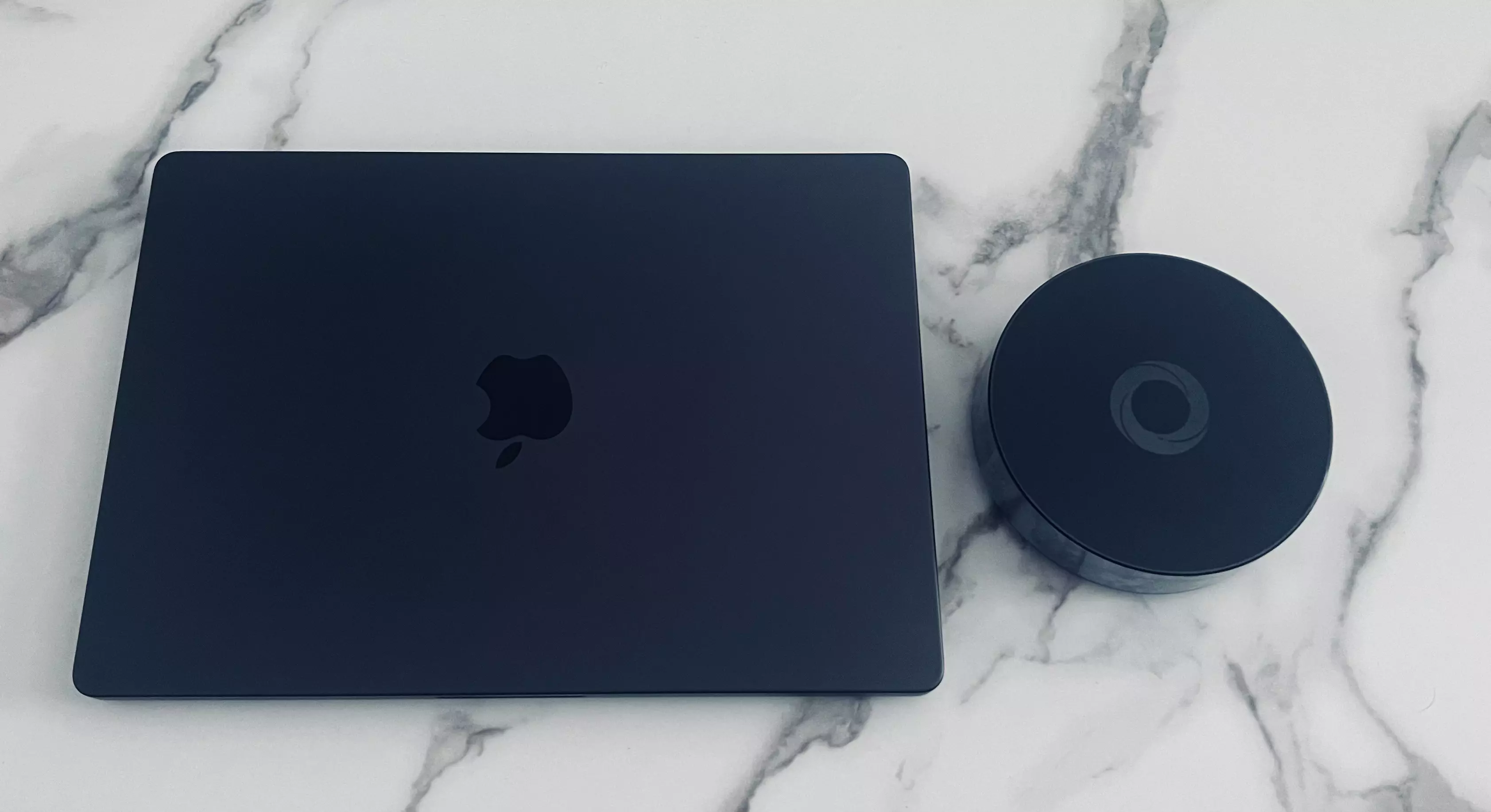 Homey Pro posé à côté d’un MacBook Pro fermé pour comparer son encombrement