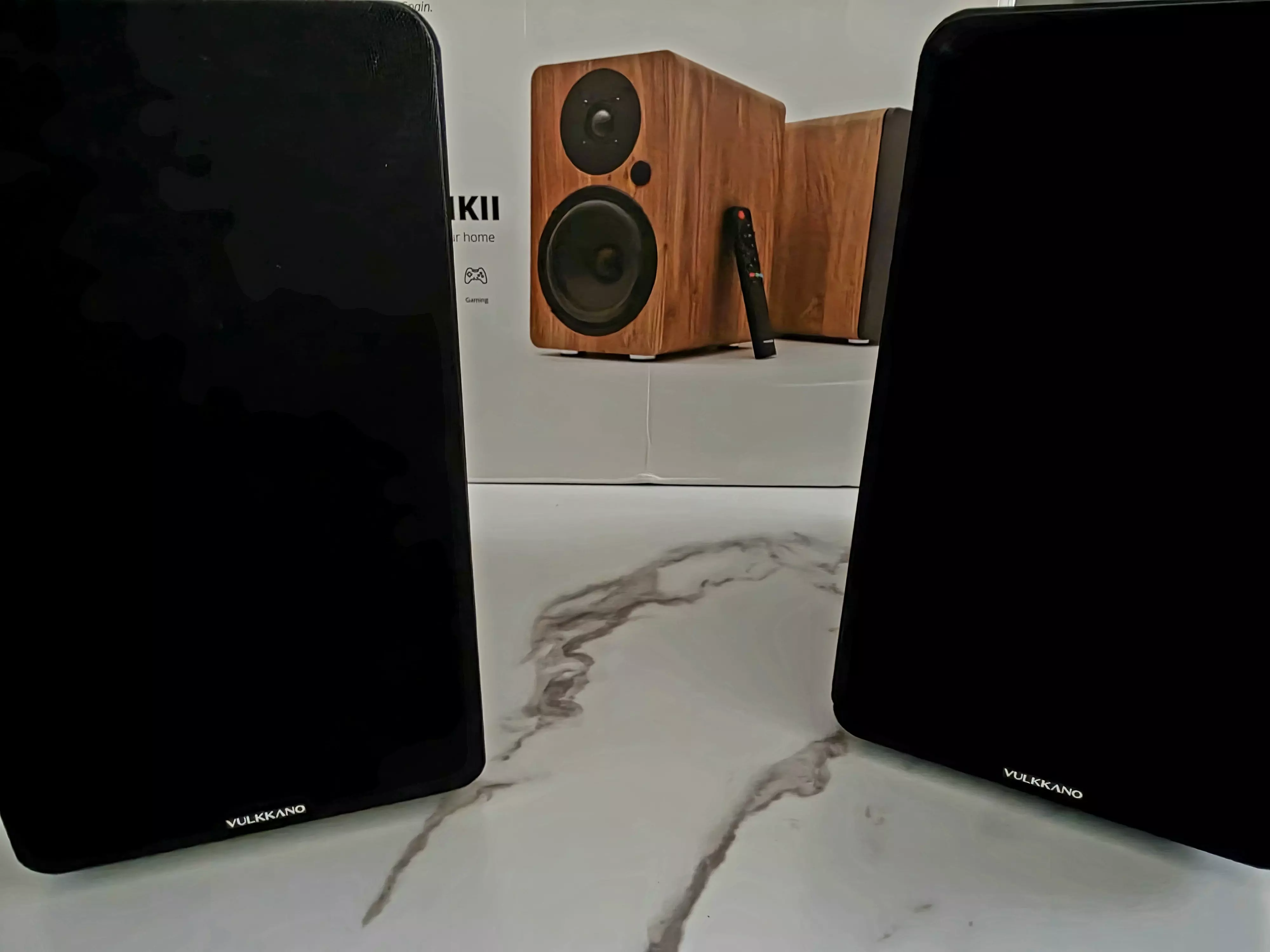 Deux enceintes VULKKANO A5 ARC MKII noires posées devant leur boîte dans un salon
