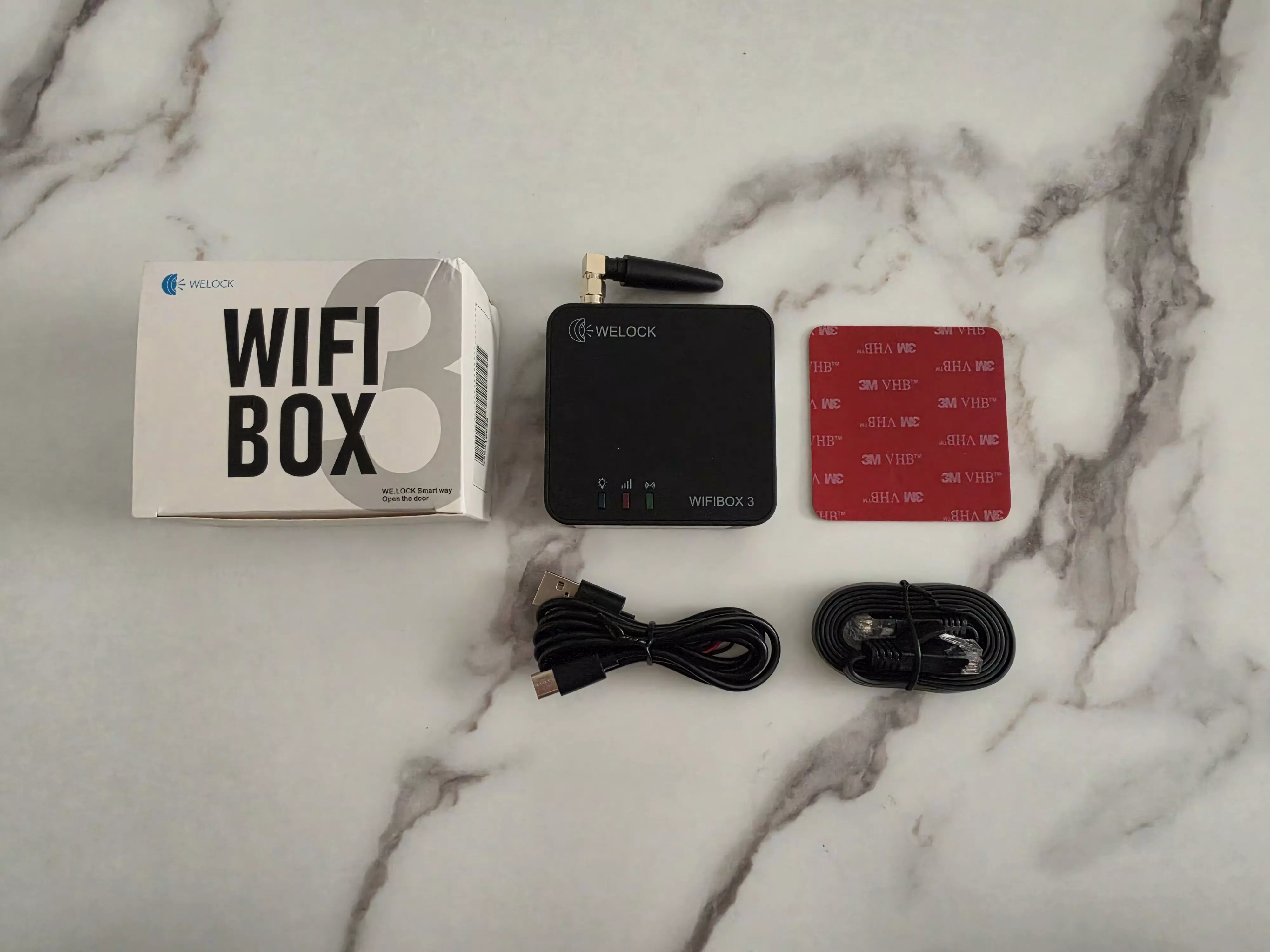 WELOCK WiFiBox3 avec sa boîte, son antenne, ses câbles USB et Ethernet et un adhésif de fixation