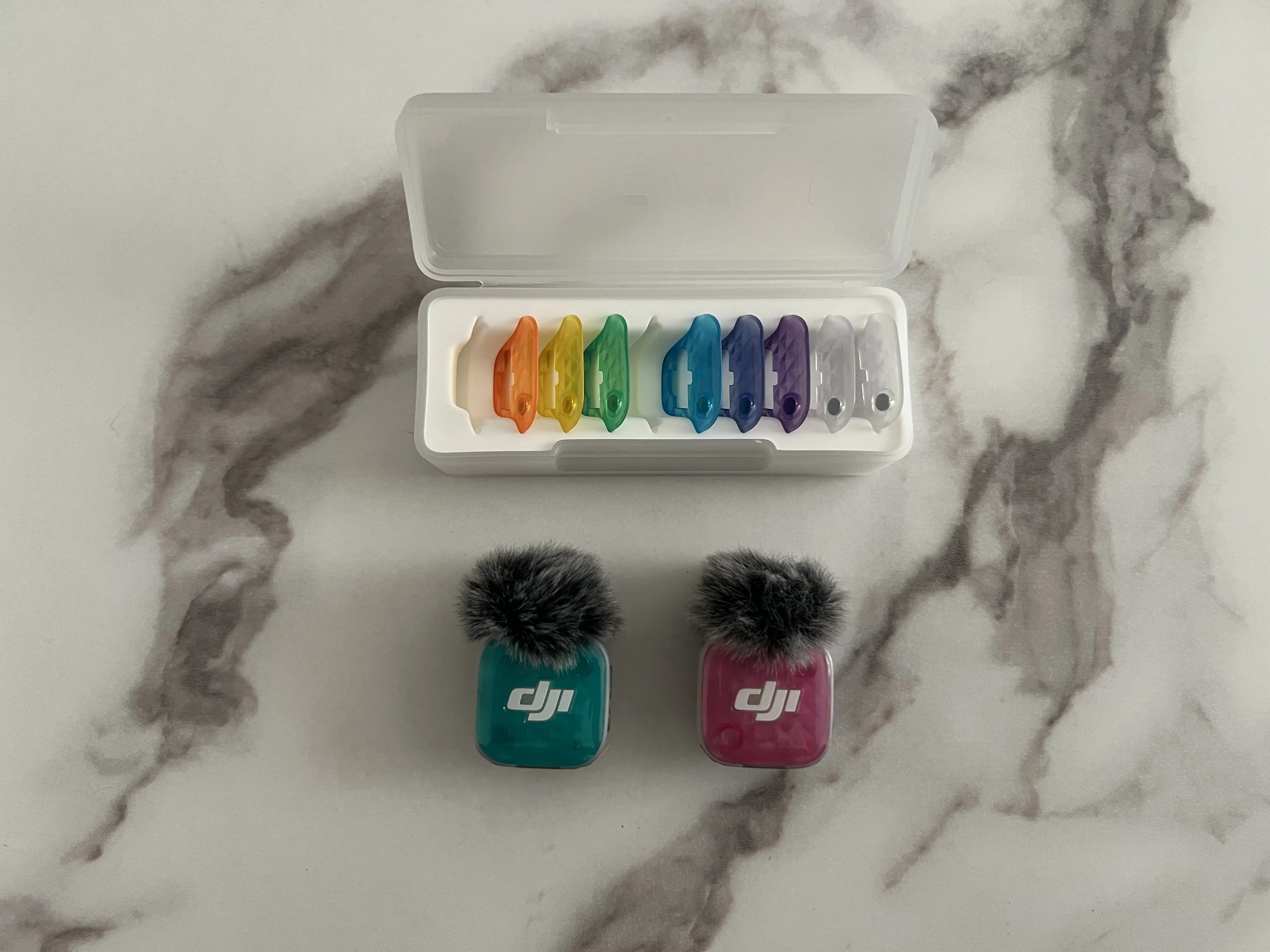 Deux émetteurs DJI Mic Mini 2S avec façades turquoise et rose sous une boîte de coques colorées