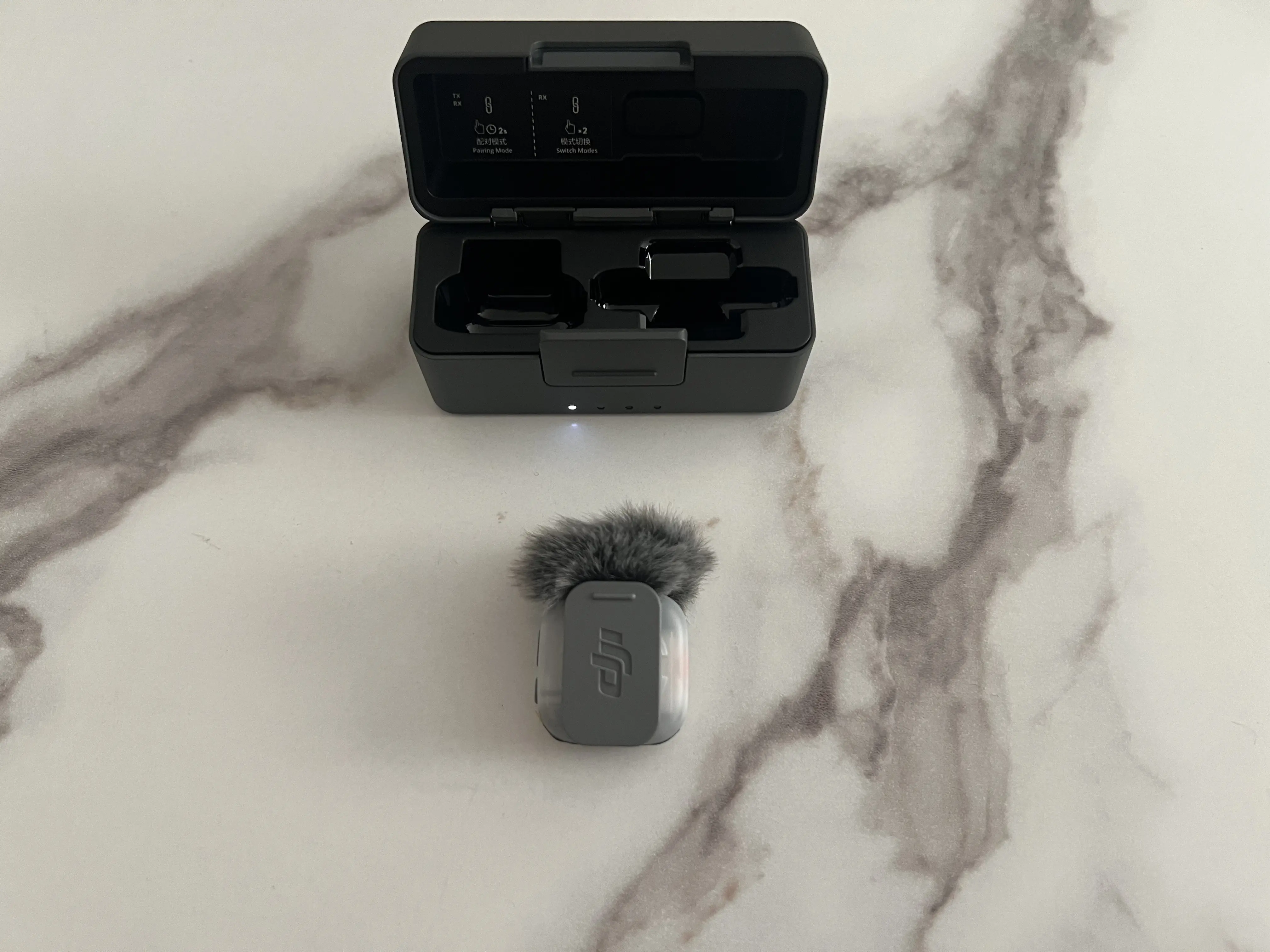 Dos d’un émetteur DJI Mic Mini 2S avec son clip amovible devant le boîtier de recharge