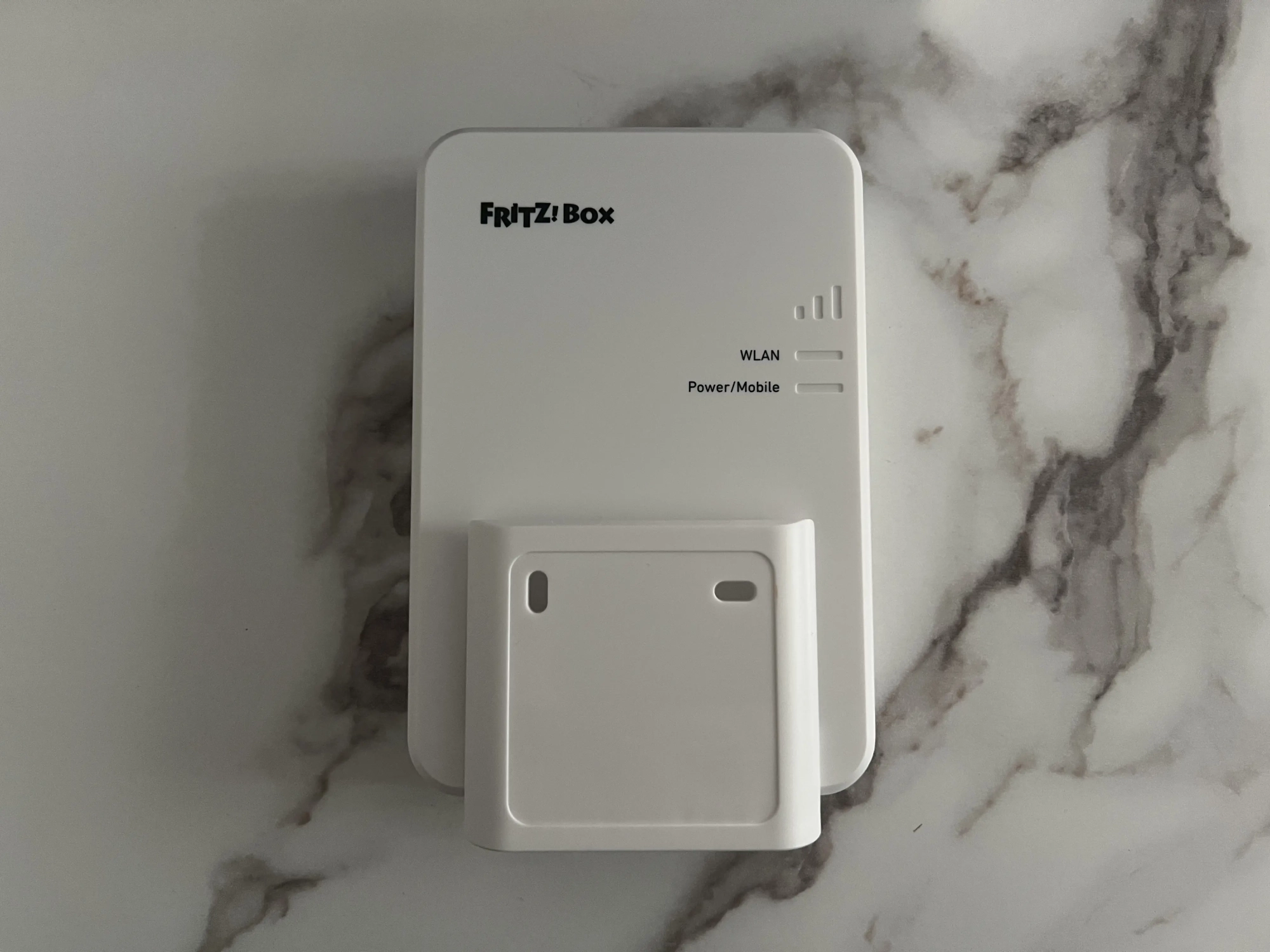 FRITZ!Box 6860 5G avec son support de montage blanc présenté devant le routeur
