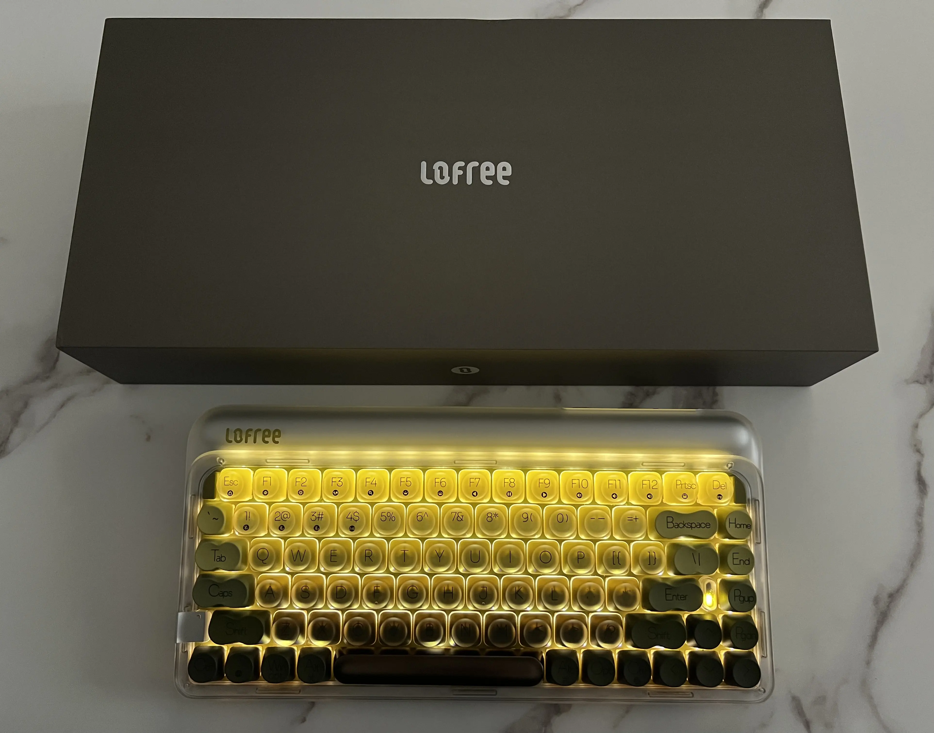 Lofree 432Hz Polar Moss illuminé en jaune sous sa boîte noire, photographié de dessus