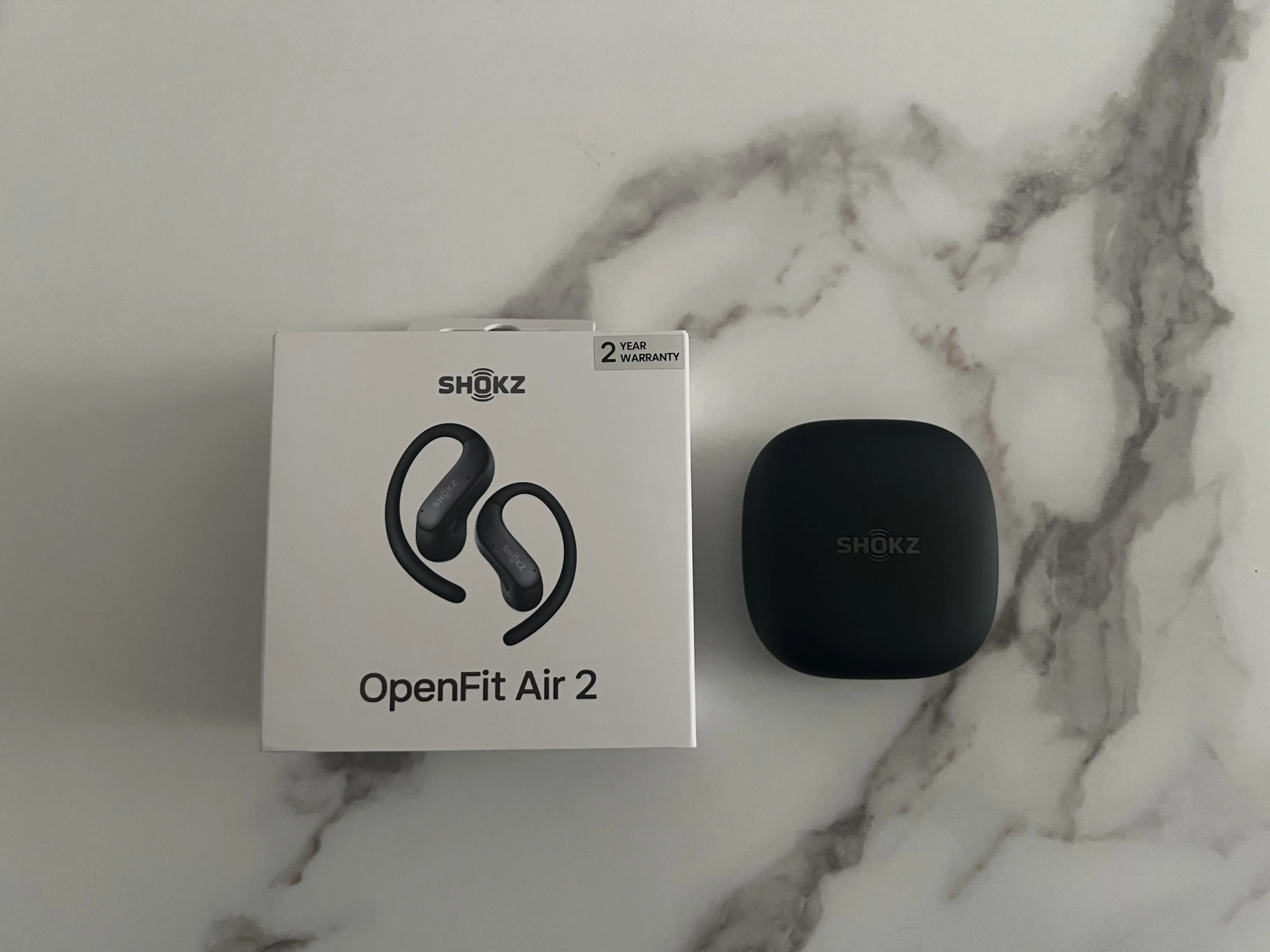 Boîte des Shokz OpenFit Air 2 posée à côté de leur étui noir fermé